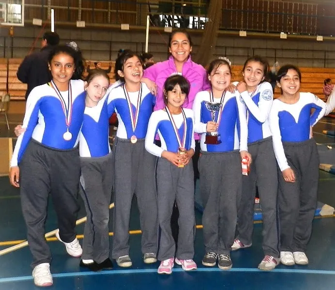 Gabriela with her young gymnastics team celebrating with medals and a trophy